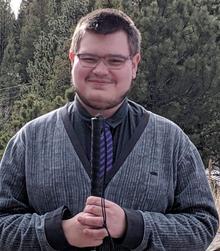 Standing outdoors, smiling, holding top of longwhite cane
