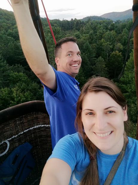 Adoption Profile Photo. Jessica and Nathan in a hot air balloon basket floating high above trees. They build and fly hot air balloons together.