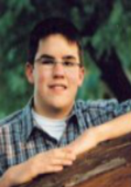 Senior picture of Daniel, with hands together on a a table that is tilted forty-five degrees with left arm above right, smiling, looking at camera.