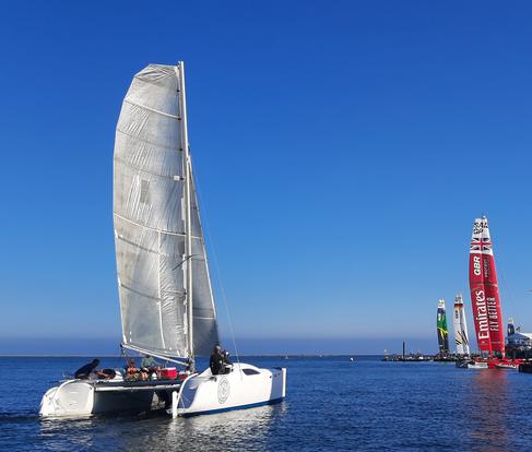 4 guys all putting up the shaka in the sand using beachtrax in front of a catamaran. Link to Waves4All Sailing Page.