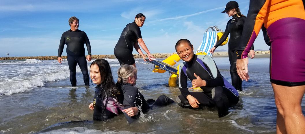 Hey whats up Josh, let me know if you hear this. This image is of a girl and guy sitting back to back in the water. She is holding him up as the waves roll over them. He is paralayzed and there are people showing up to help. One girl with super short hair is throwing up a shaka!