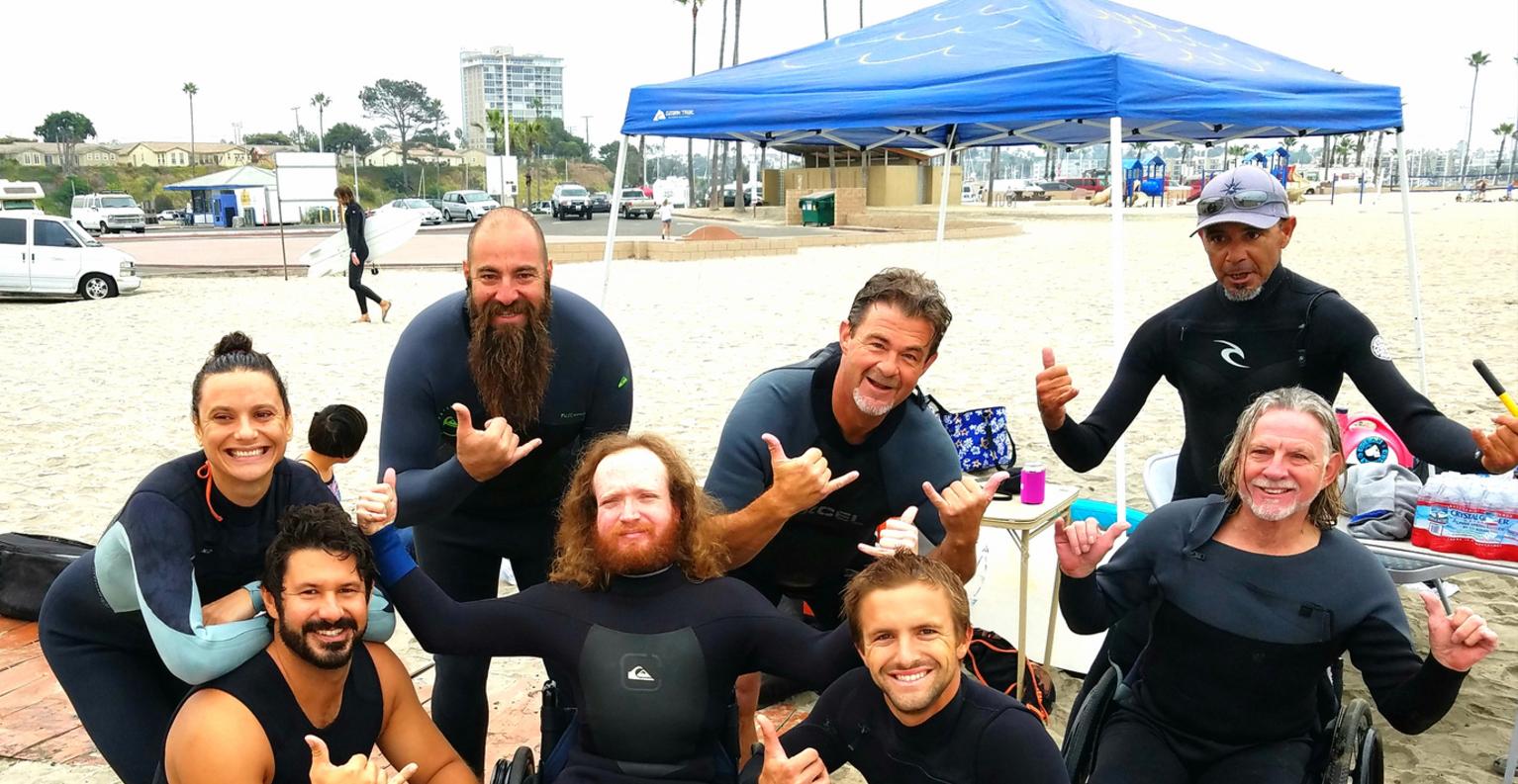 Picture of a people about to go surfing, a man holding a surfboard with a women holding his shoulder with a young girl all standing in the whitewater as waves roll in towards them.