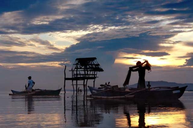 Southeast Asia men on small wooden boat, one with a net over his shoulders