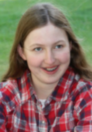 Outdoor picture of Hannah, wearing a plaid shirt, smiling and looking at the camera.