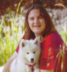 Outdoor picture of Ashley holding her dog, smiling, looking at the camera.