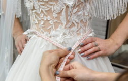 seamstress measuring a womans waist for bridal gown.