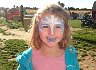 A young girl with a snowflake crown painted on her forehead and blue lipstick.