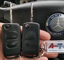 2 Mercedes flip keys next to each other in front of a Mercedes steering wheel with an Autotechnix key ring attached to 1 of the keys