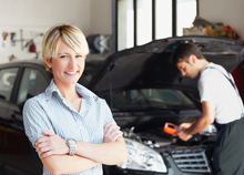 Woman smiling in a blue shirt while someone changes oil in a car