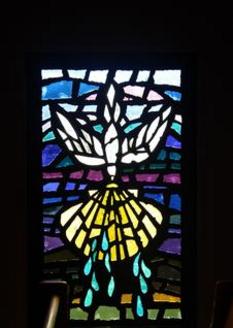 Stained glass window representing the Sacrament of Bapitsm. The window contains a white dove coming down from Heaven holding a large seashell with blue water droplets coming off the shell.