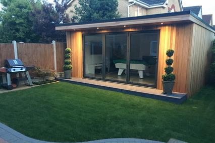 Modern cedar clad garden room with 3 panel bifold doors and topiary trees either side